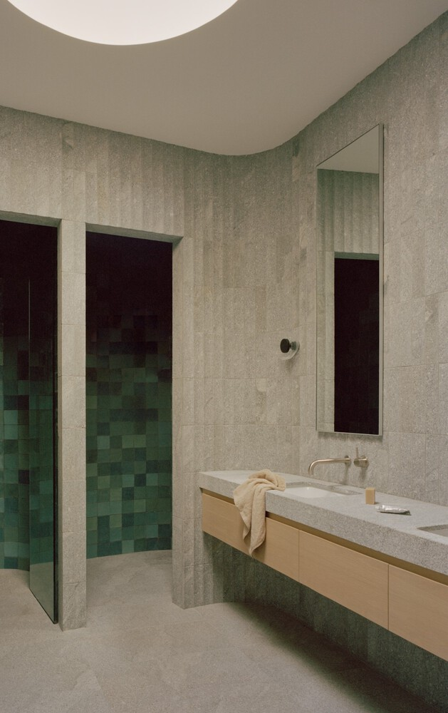 Bathroom with green mosaic tile shower enclosure and floating oak vanity beneath curved plaster ceiling