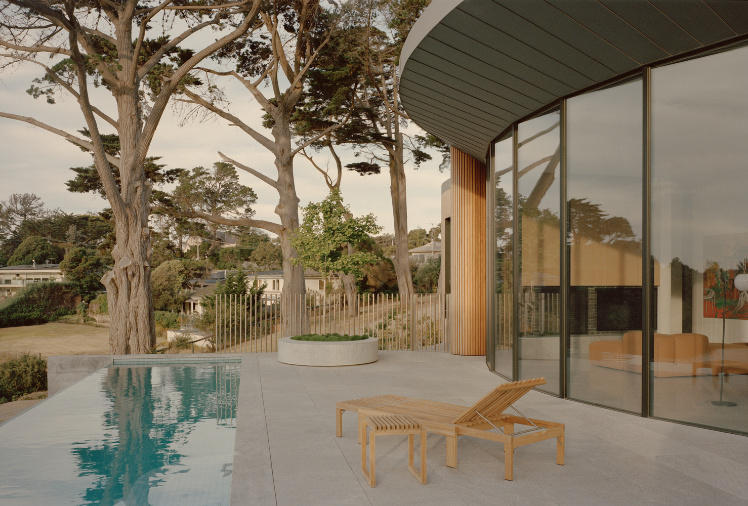 Poolside terrace with full-height glazing and eucalyptus trees under overcast sky