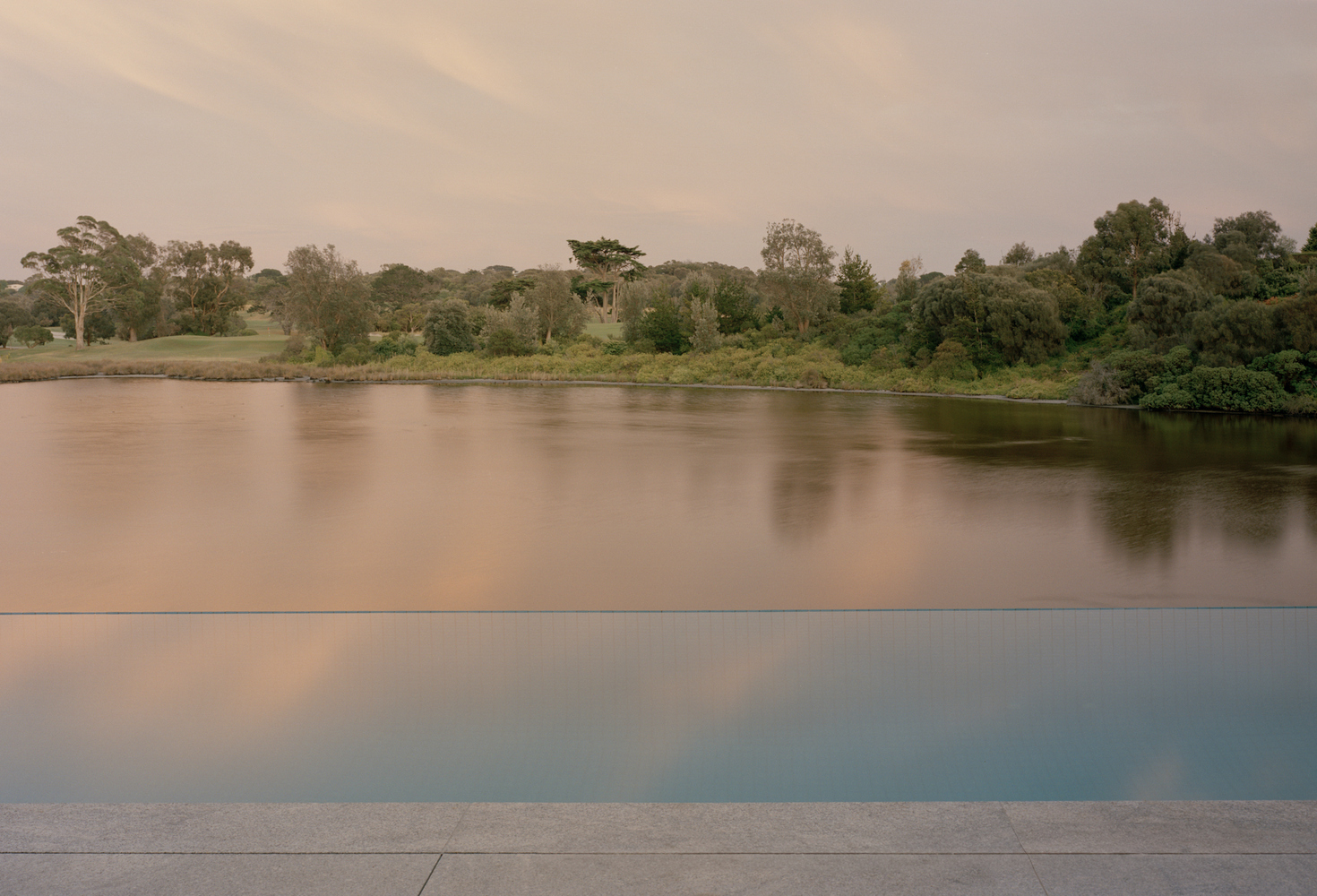 Infinity pool edge reflecting the river and distant treeline at dusk