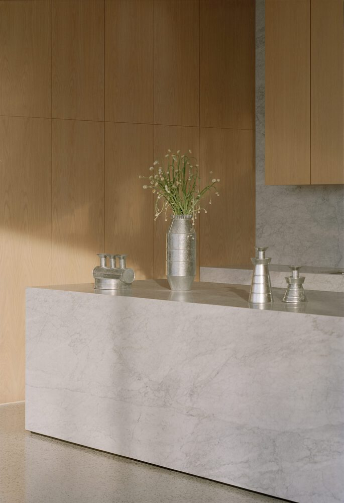 White marble island against oak paneled walls with silver vessels and delicate flowers