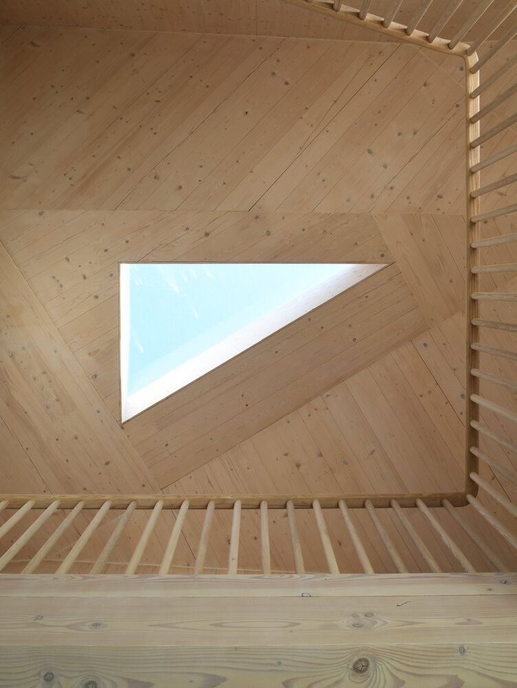 Upward view of stairwell with triangular skylight cut into diagonal plywood paneled ceiling