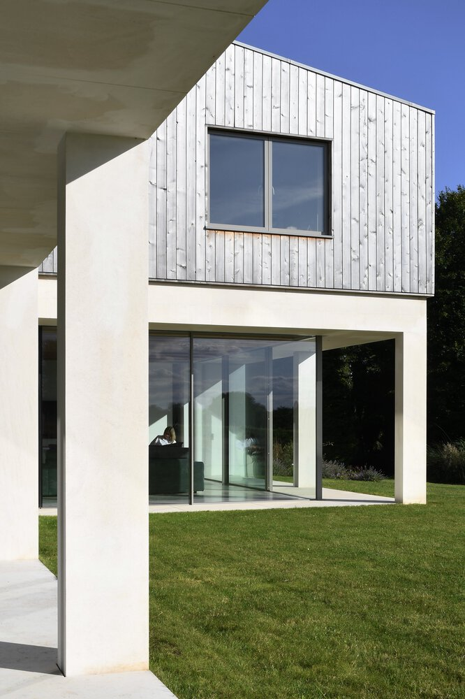Garden facade with white render ground floor and vertical timber cladding upper volume under a blue sky