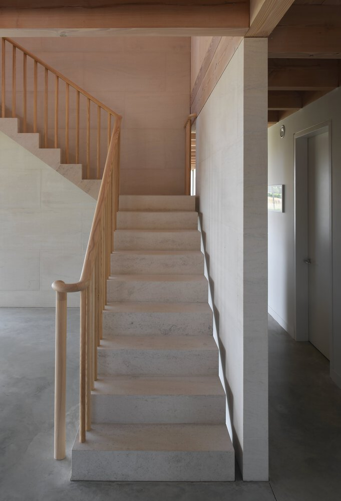 Interior staircase with pale timber treads and vertical balustrade rising alongside white plaster walls
