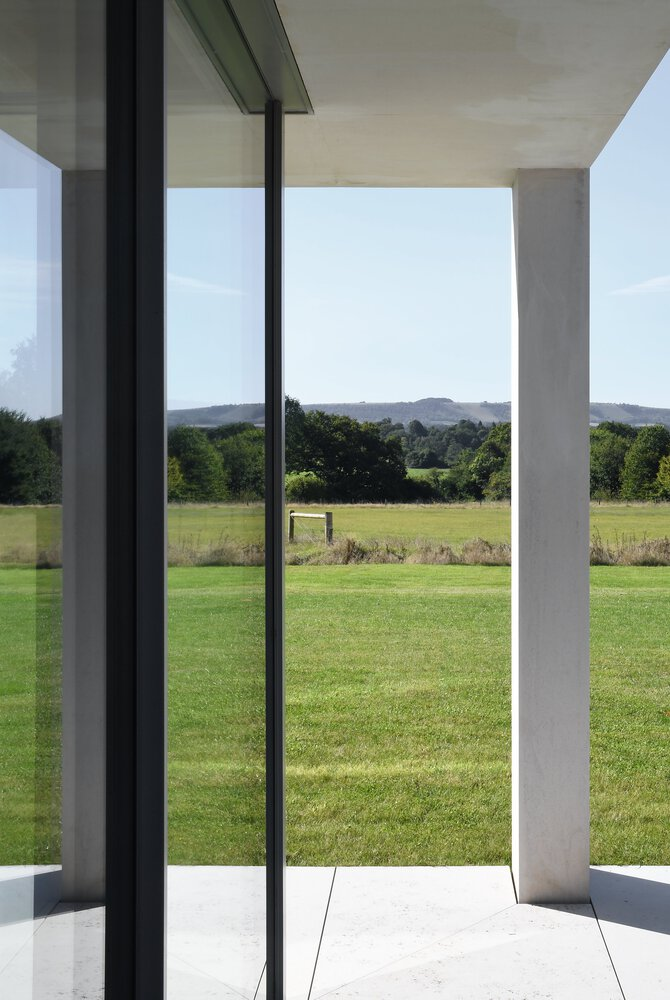 View through the glazed corner opening framing the lawn and distant hills under a clear sky
