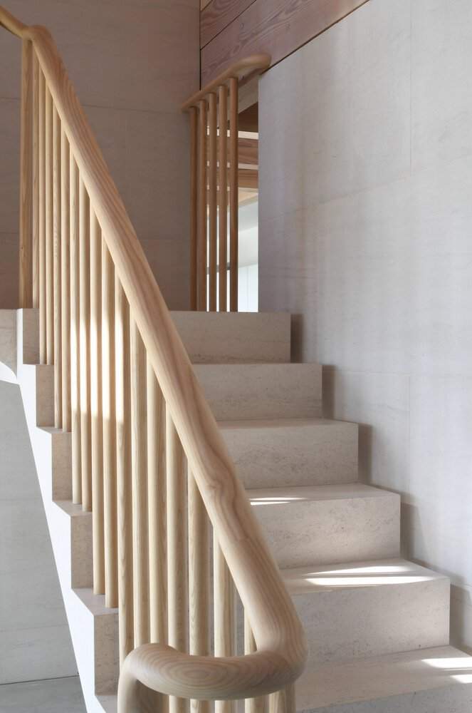 Terrazzo stair ascending between timber handrail and vertical slat balustrade with sunlight filtering through