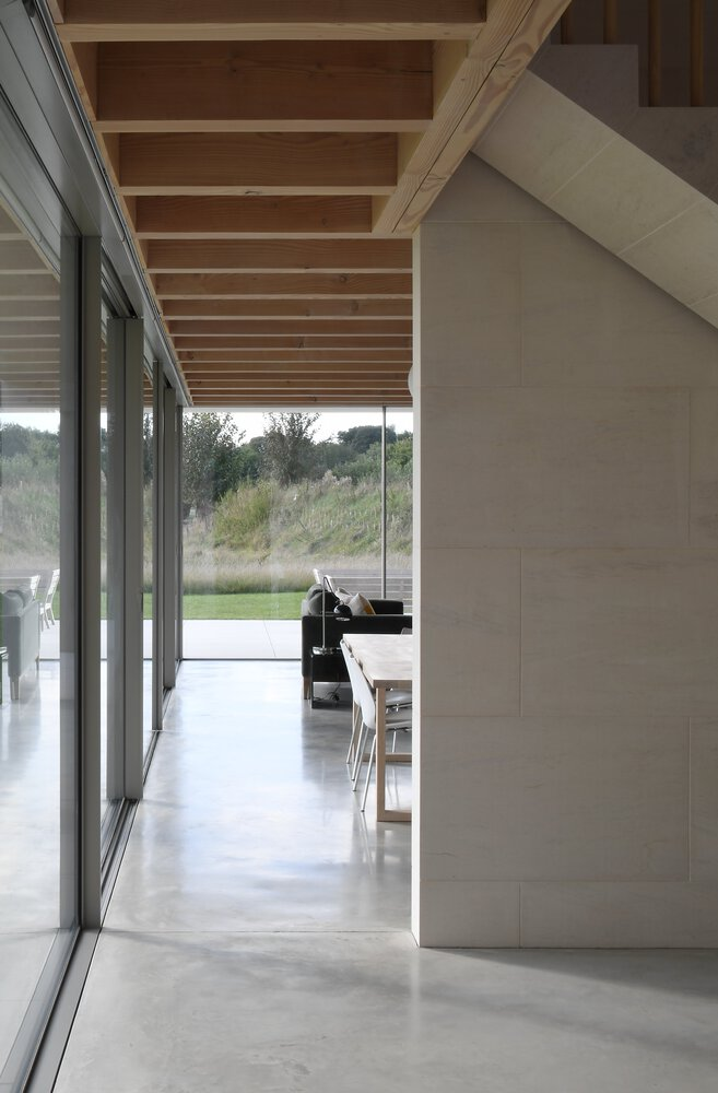 Interior corridor with exposed timber ceiling joists, glass wall overlooking lawn and dining furniture