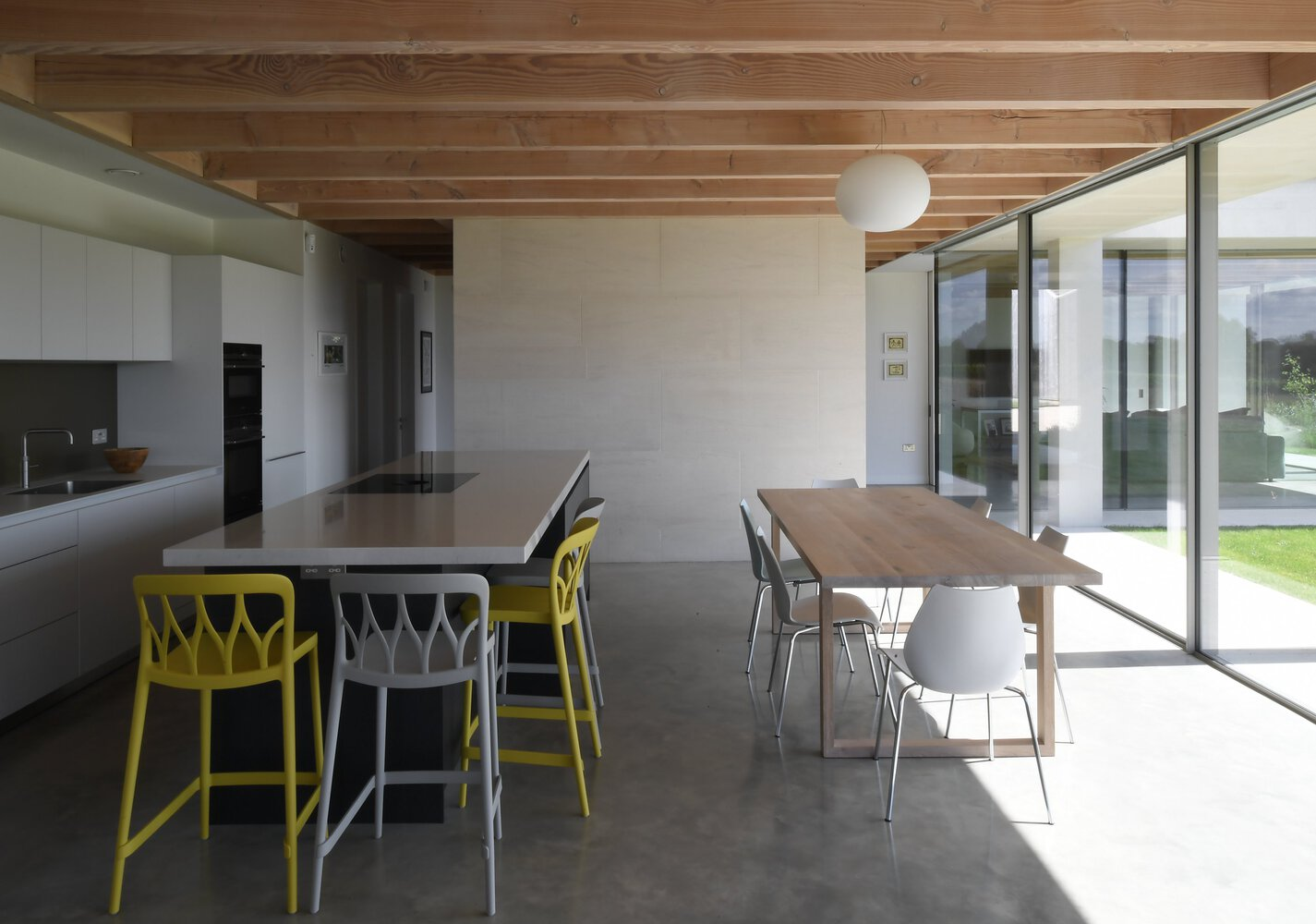 Open-plan kitchen and dining area with polished concrete floor, exposed timber ceiling and glass wall to garden