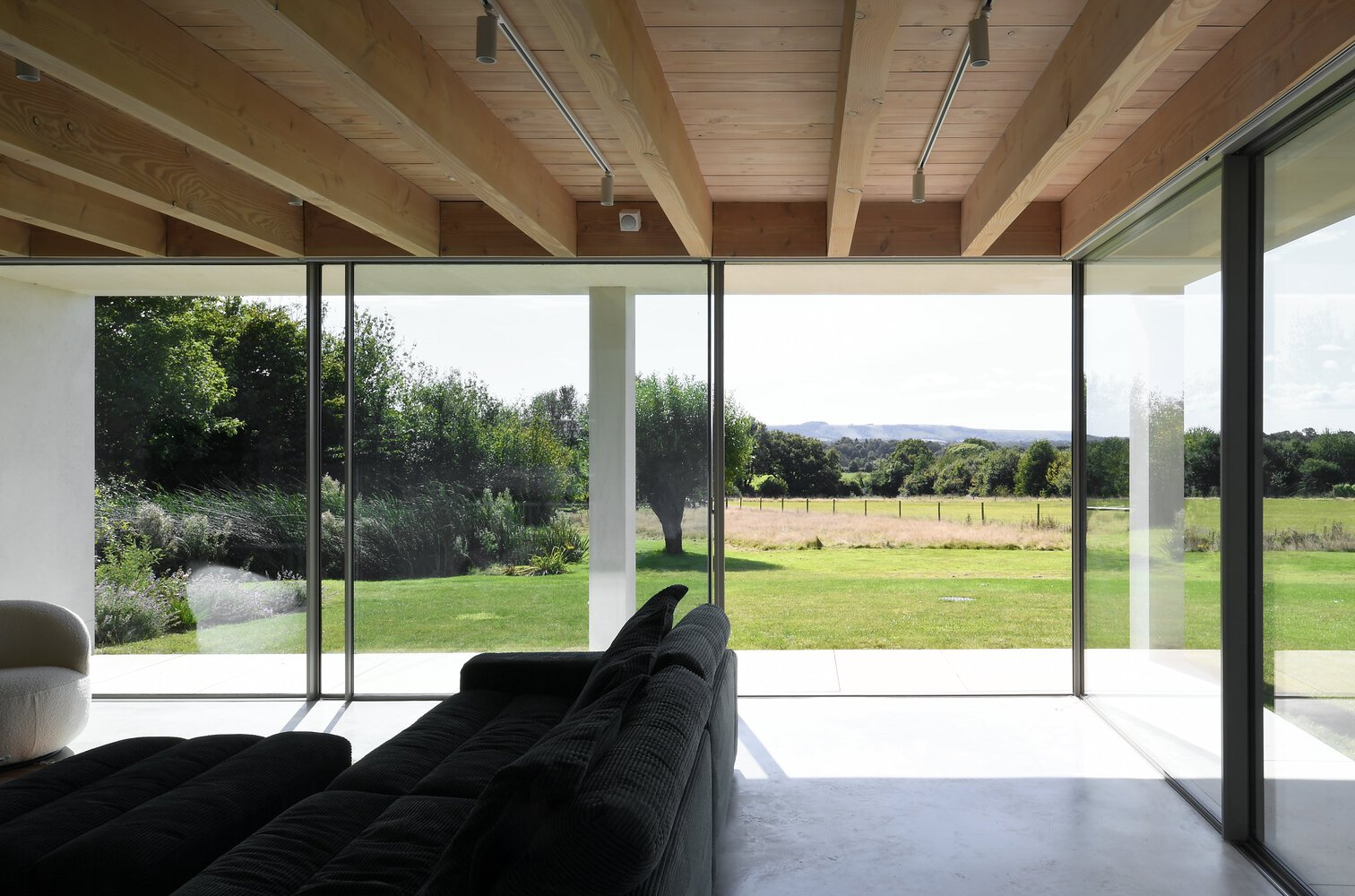 Living room with exposed timber beams and floor-to-ceiling glass doors opening to a green lawn