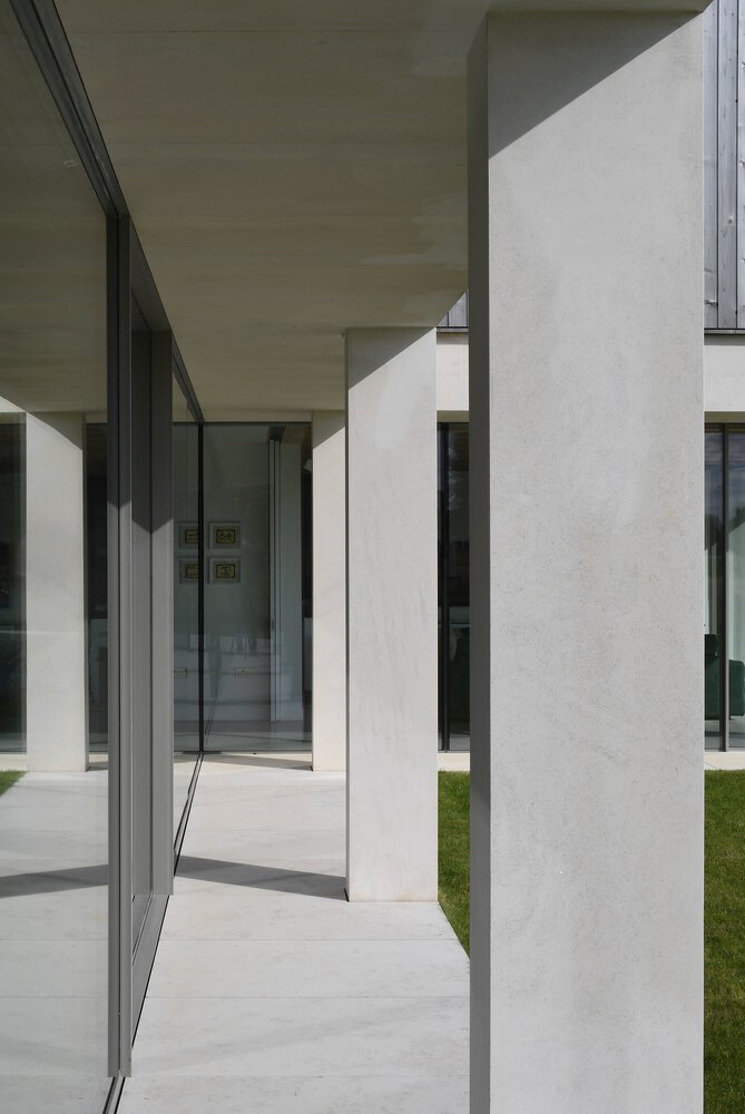 Covered walkway framed by white plaster columns and timber soffits casting hard shadows in daylight