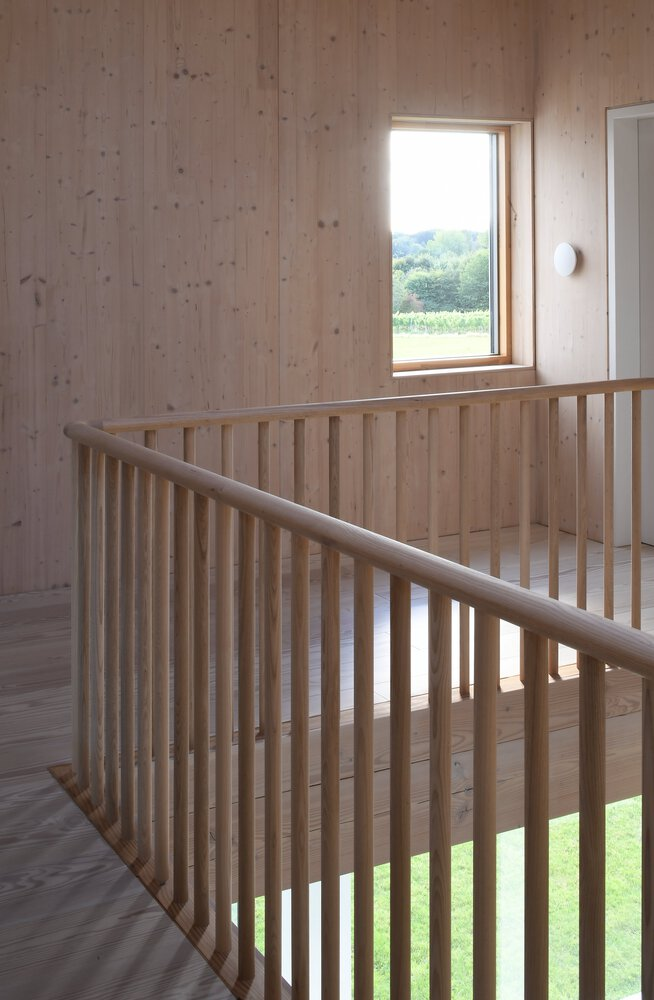 Timber stair landing with vertical balustrade slats and a window framing distant trees