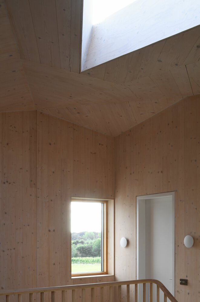 Corner of a timber-lined room with a skylight above and a narrow window overlooking fields