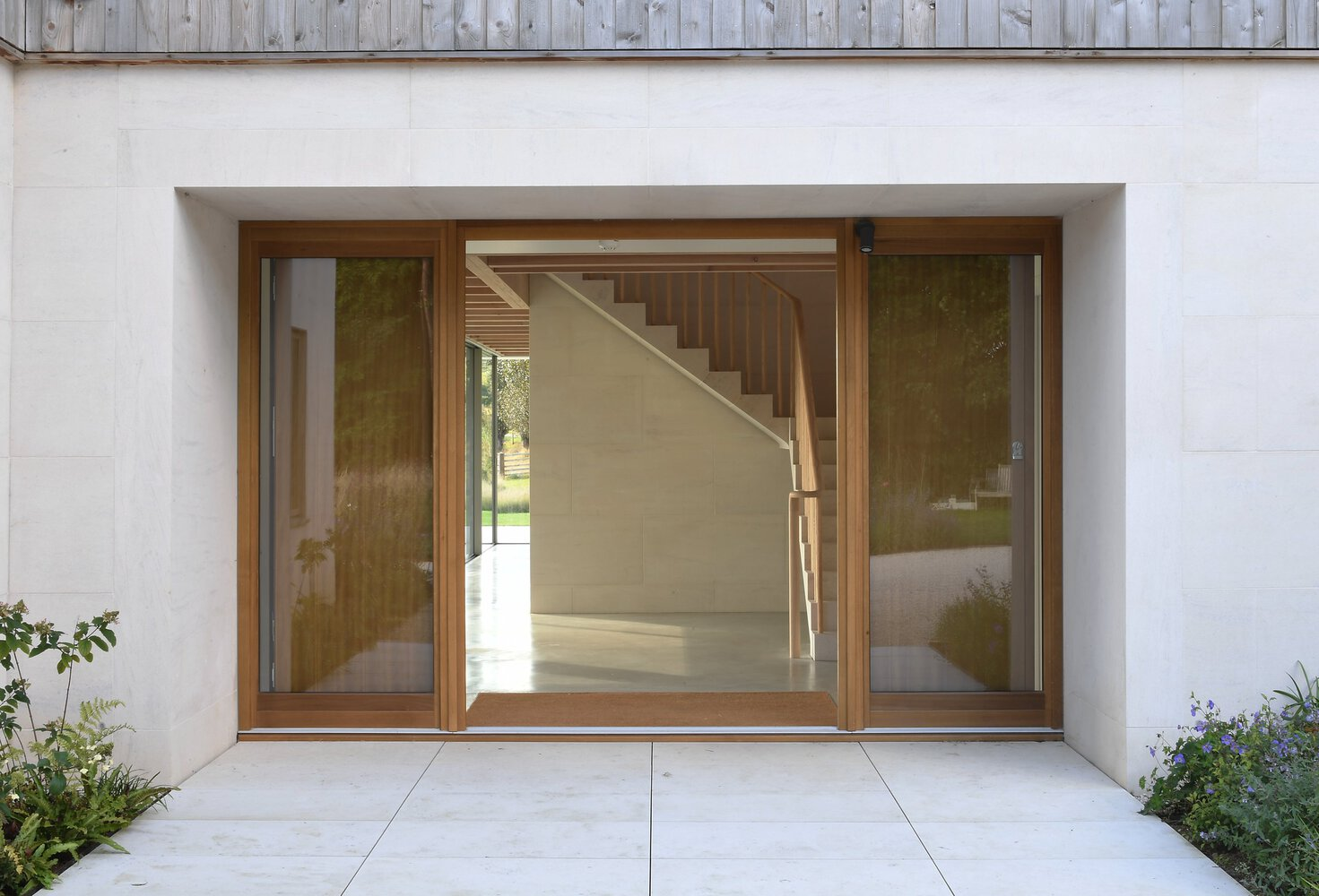 Recessed entrance with timber-framed glazed doors revealing a plywood staircase in the foyer