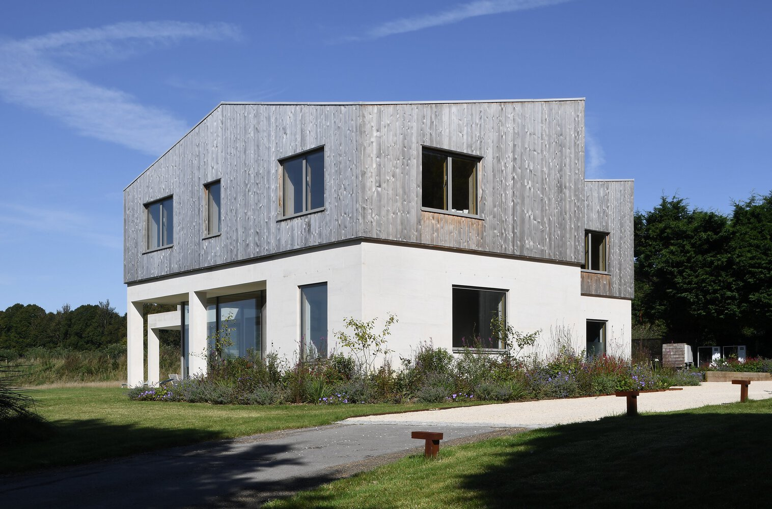 Two-story house with weathered timber cladding above white rendered walls in a lawn setting
