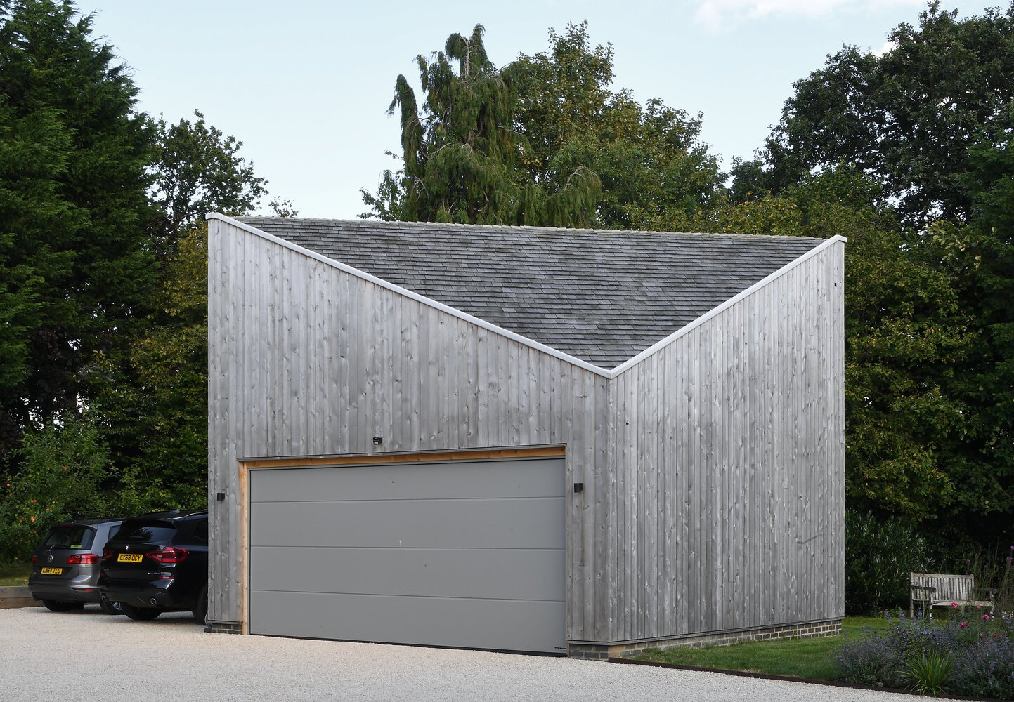 Garage block with inverted V-shaped roof clad in weathered vertical timber boarding under trees