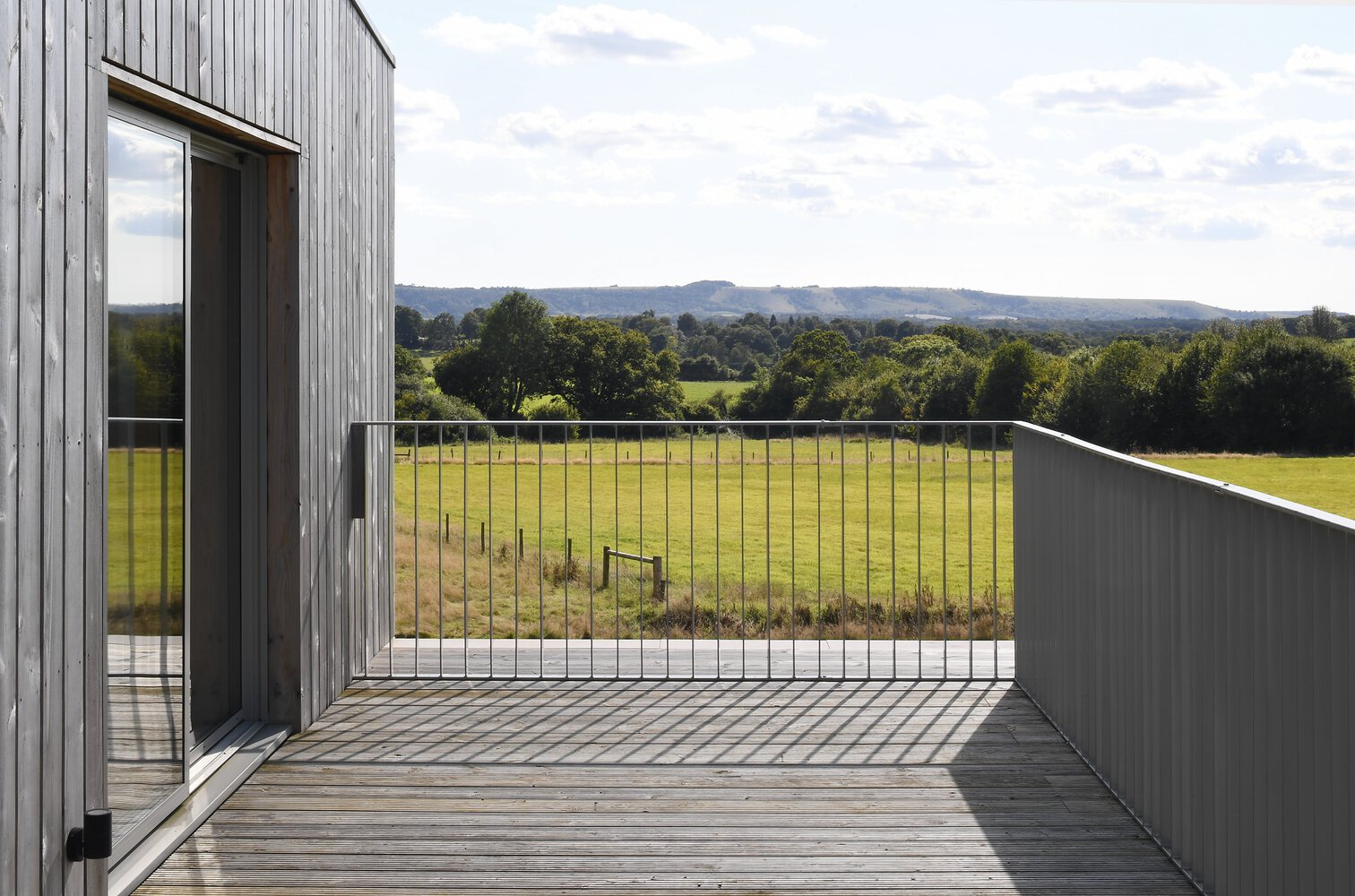 Timber deck with glass and metal balustrade overlooking rolling countryside under partly cloudy skies