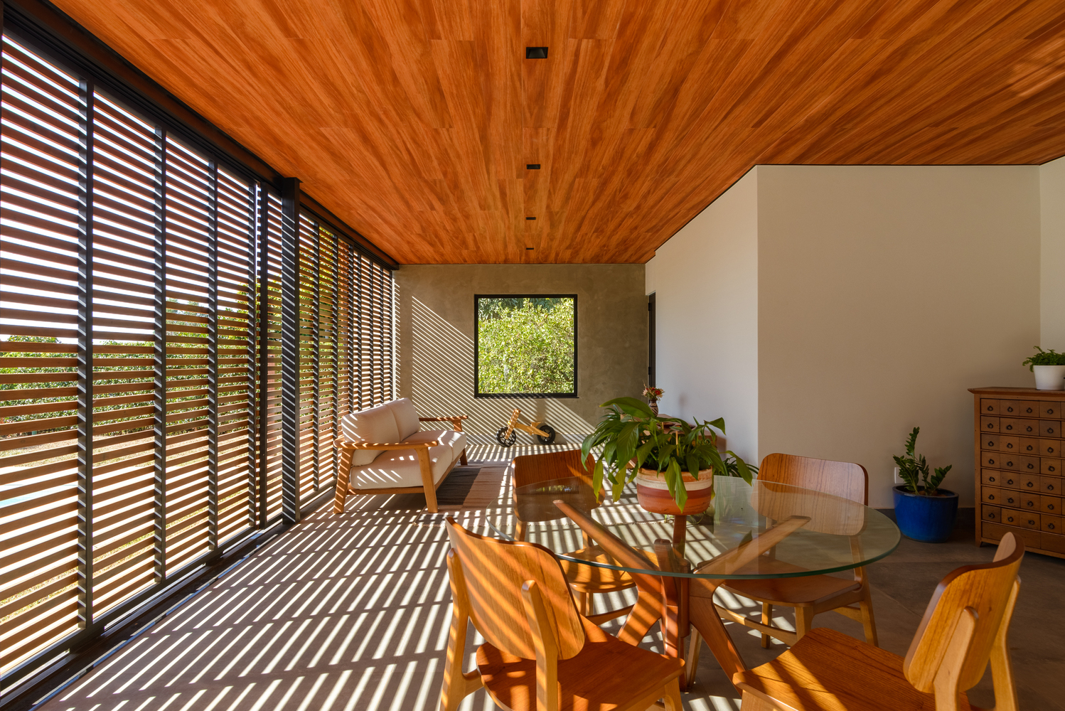 Dining area with horizontal timber louvers casting striped shadows across the concrete floor and wood ceiling