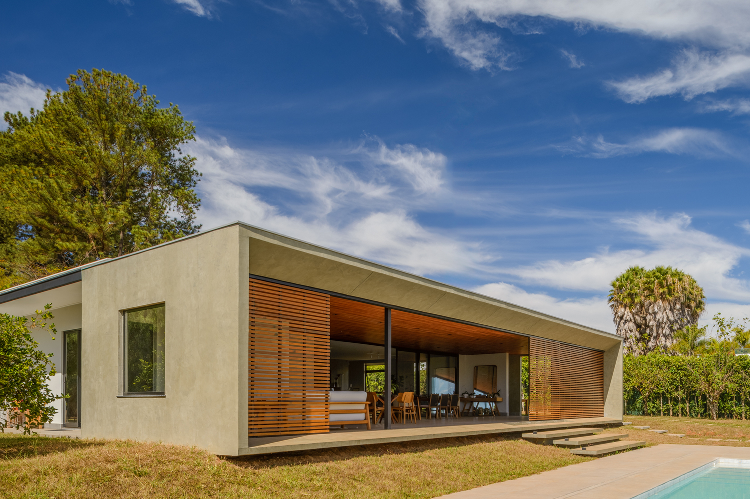 Low-pitched roof form with horizontal timber louvers spanning the facade under a blue sky