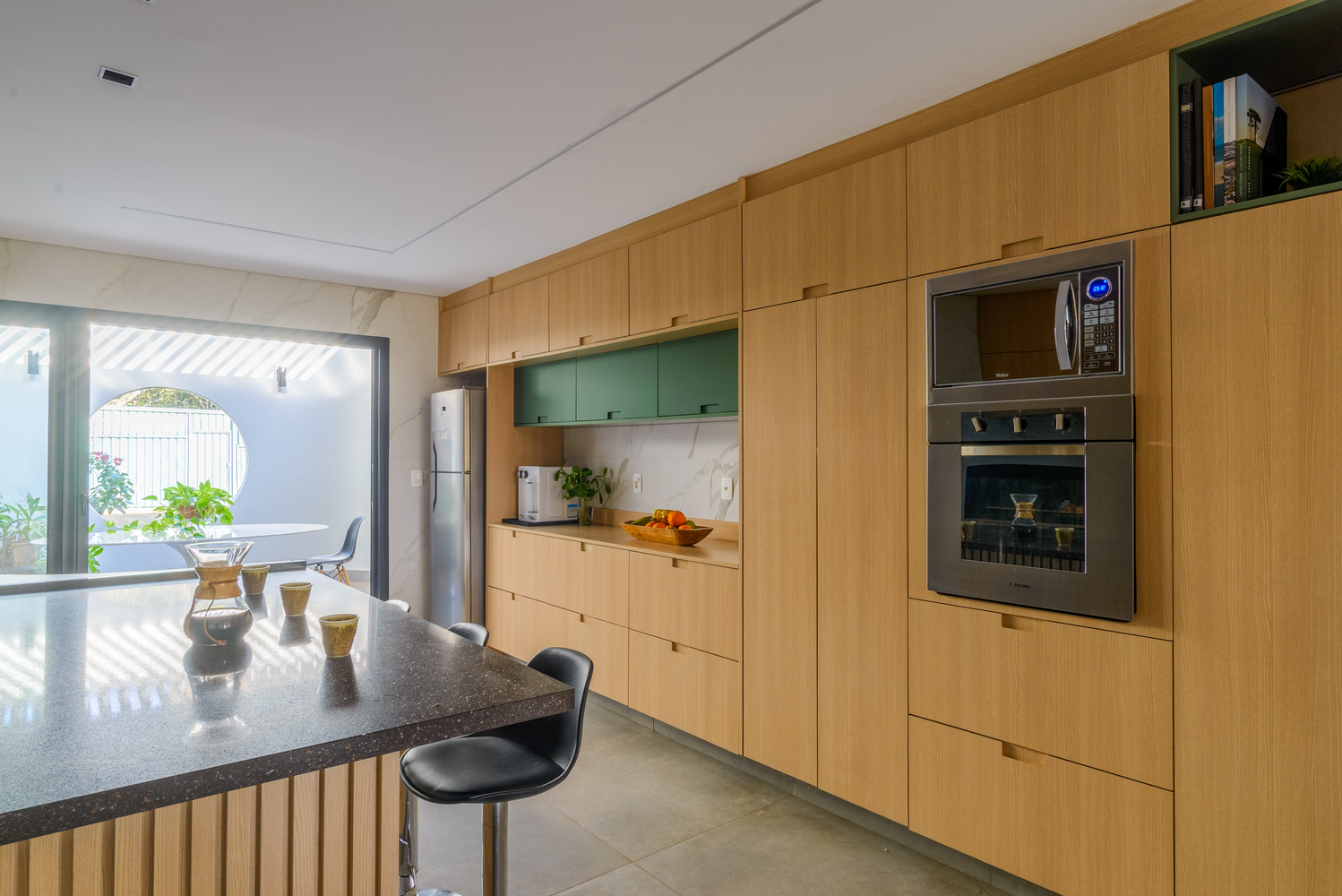 Kitchen with light timber cabinetry and view through window to arched opening in courtyard