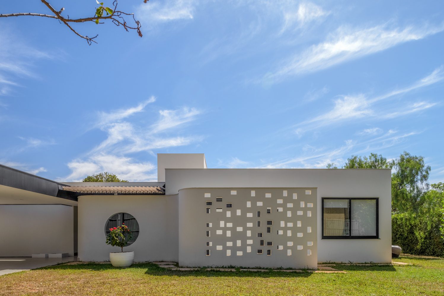 Garden facade with white stucco, scattered square windows, and a circular portal framed by lawn and trees