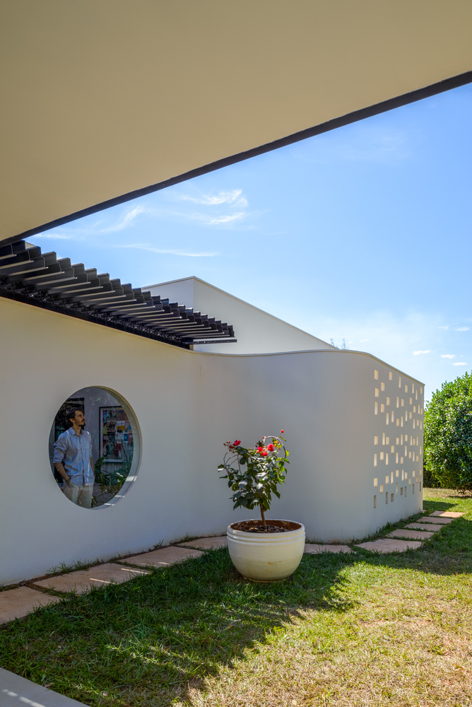 White stucco wall with circular window and perforated screen openings beside a potted rose