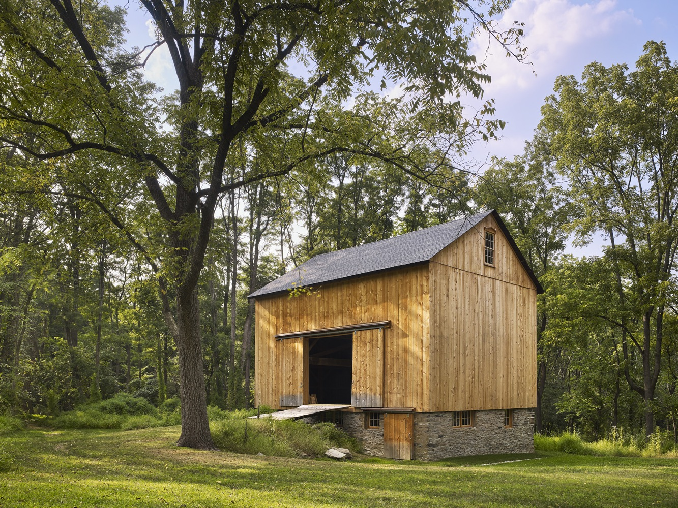 Gabled structure with vertical wood siding on a stone plinth with a person seated in the threshold