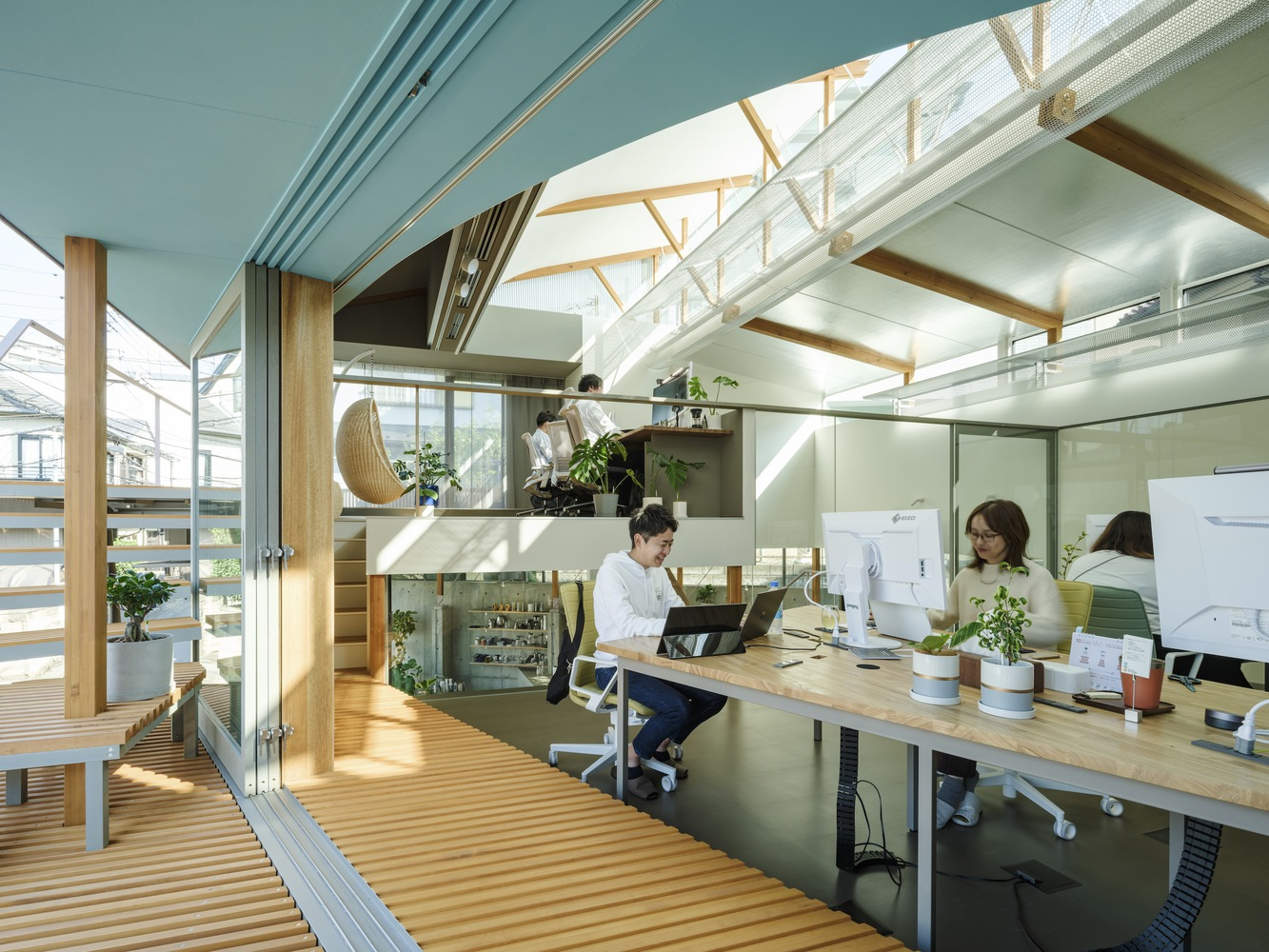 Interior workspace with exposed timber trusses, perforated metal ceiling panels and occupants at desks beneath skylights