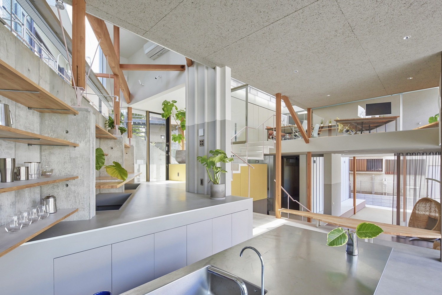 Open kitchen and living area with exposed diagonal timber bracing, split levels and concrete surfaces beneath clerestory glazing
