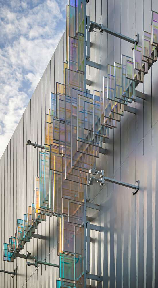 Close-up of the dichroic glass cross with iridescent panels mounted on steel armature against ribbed cladding