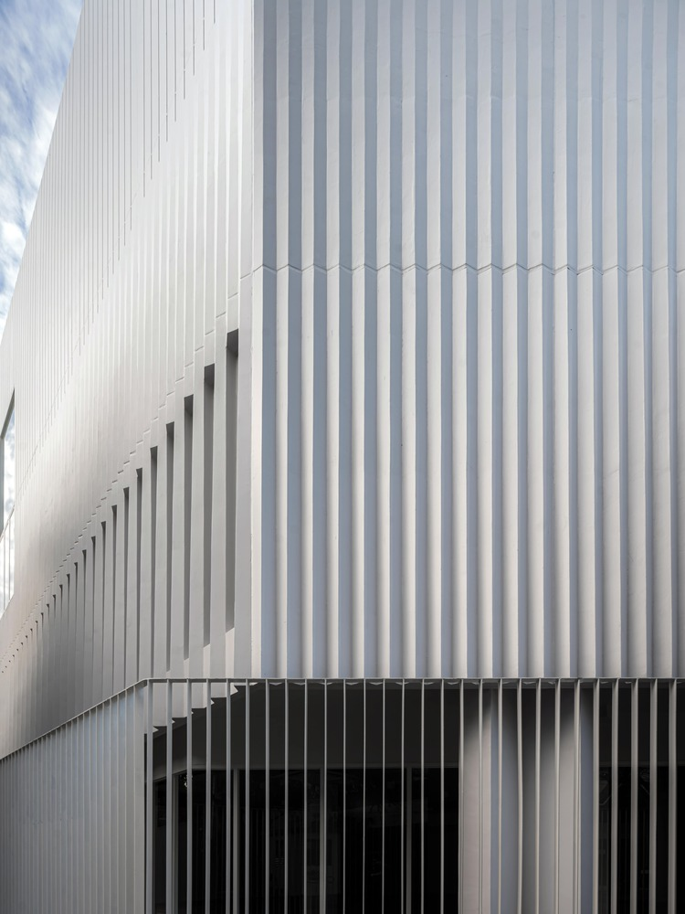 Detail of the white corrugated metal facade with vertical slot openings and dark horizontal base screening