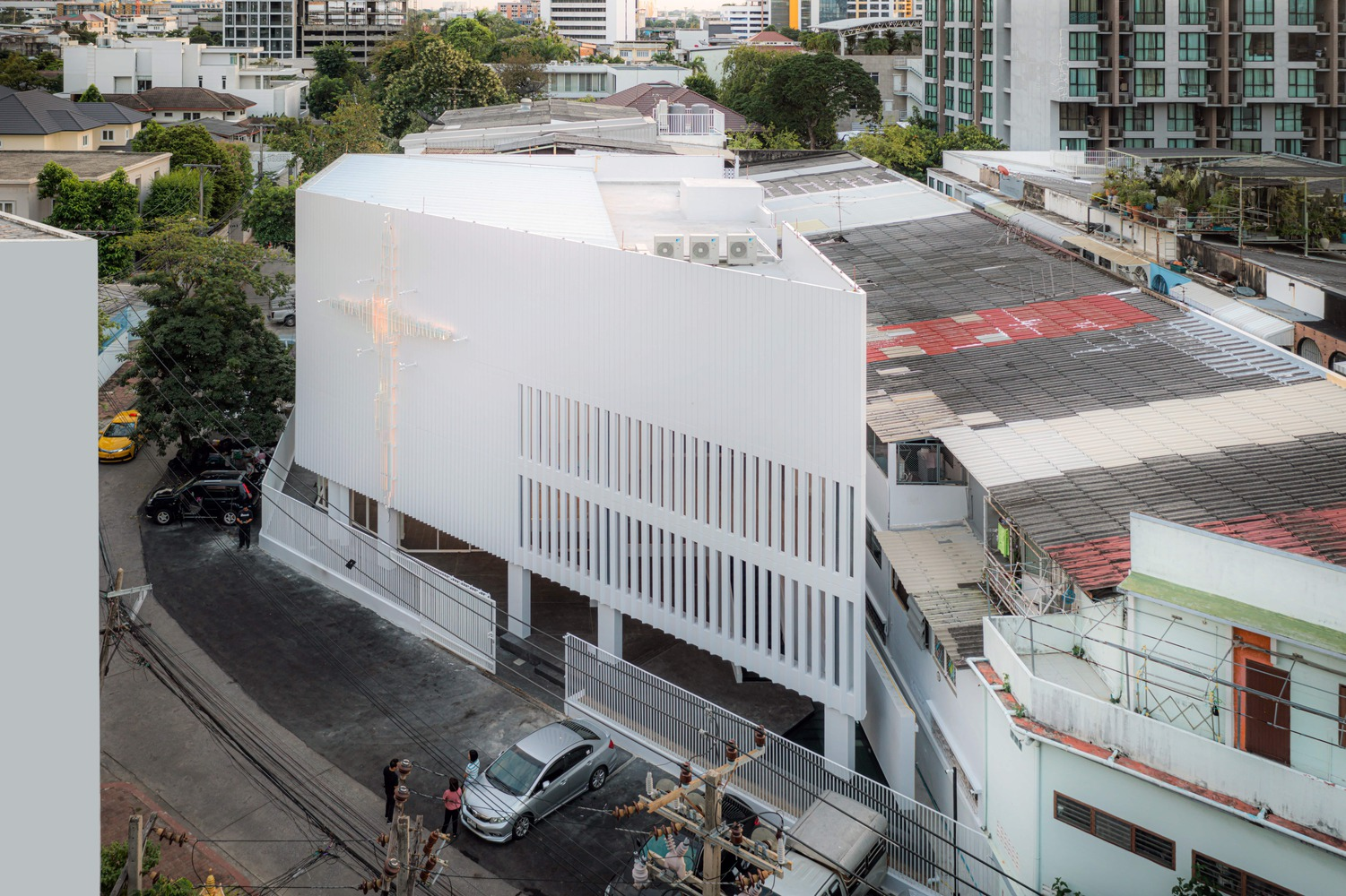 Aerial view showing the white box volume with vertical louvers on rooftop adjacent to parking area