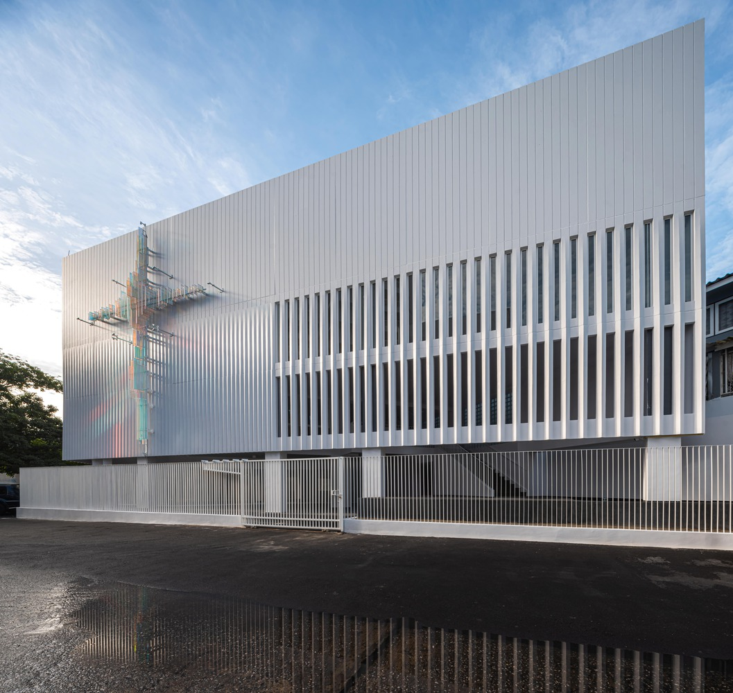 Elevation of the ribbed white facade with vertical fin screen and wet pavement reflection at dusk