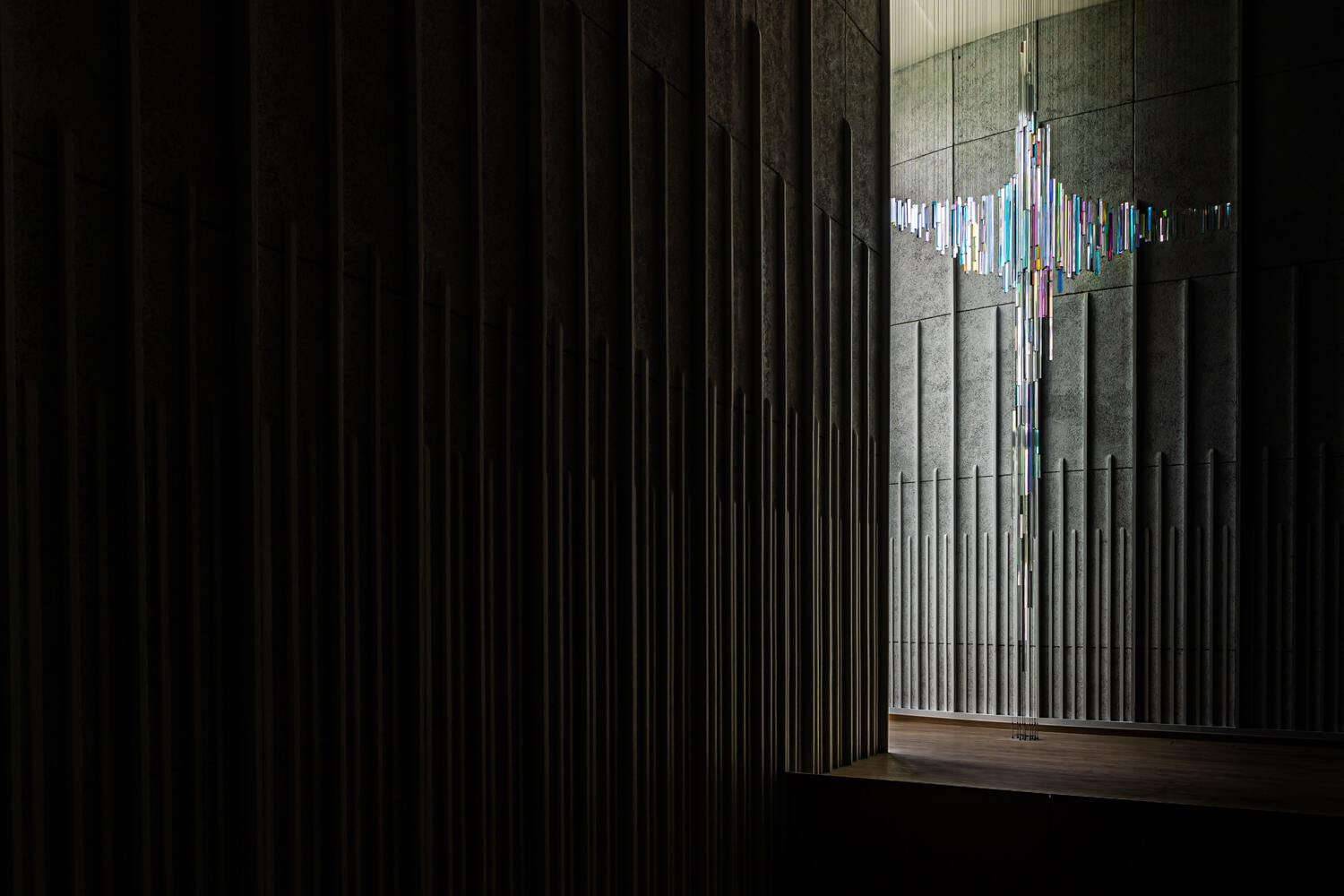 Dark interior with vertical timber battens and a glimpsed chandelier through an opening