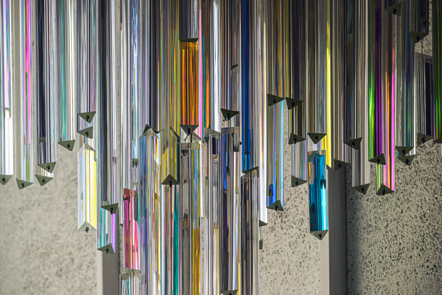 Detail of multicolored glass tubes suspended vertically against a textured concrete wall