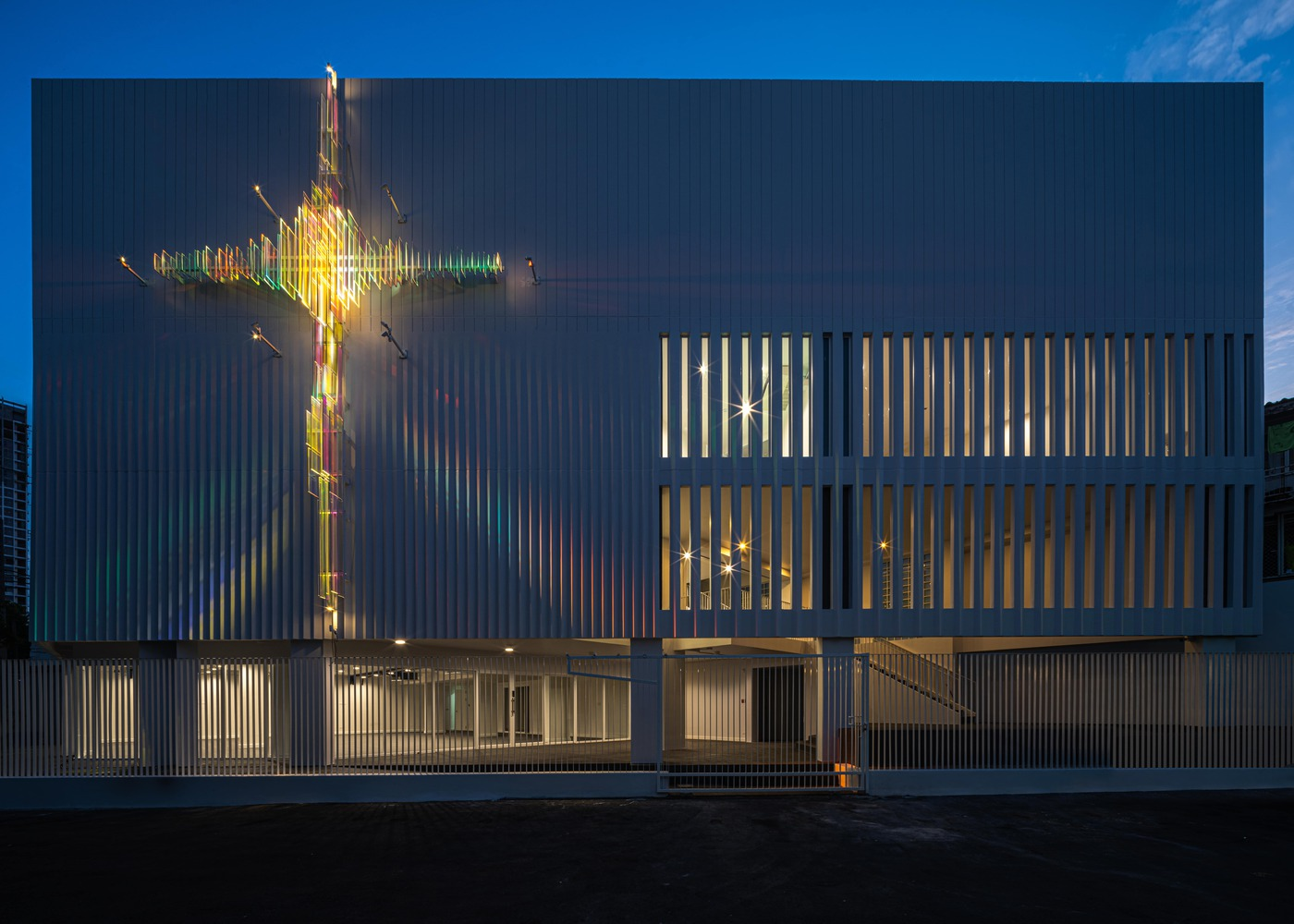 Street view of the vertical louver facade with glowing cross and entrance at night