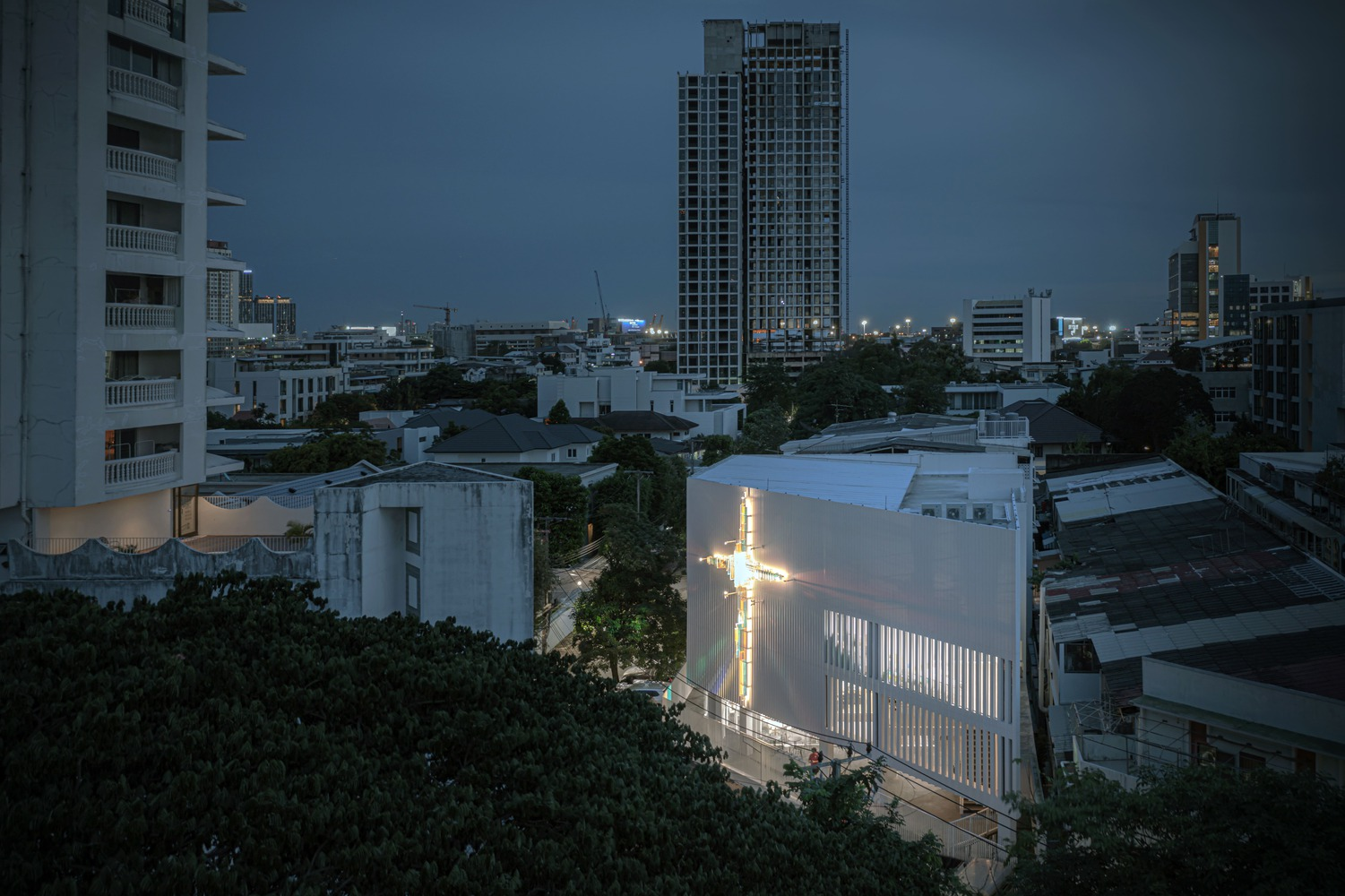 Elevated view of the illuminated cross on the corrugated facade at dusk among surrounding buildings