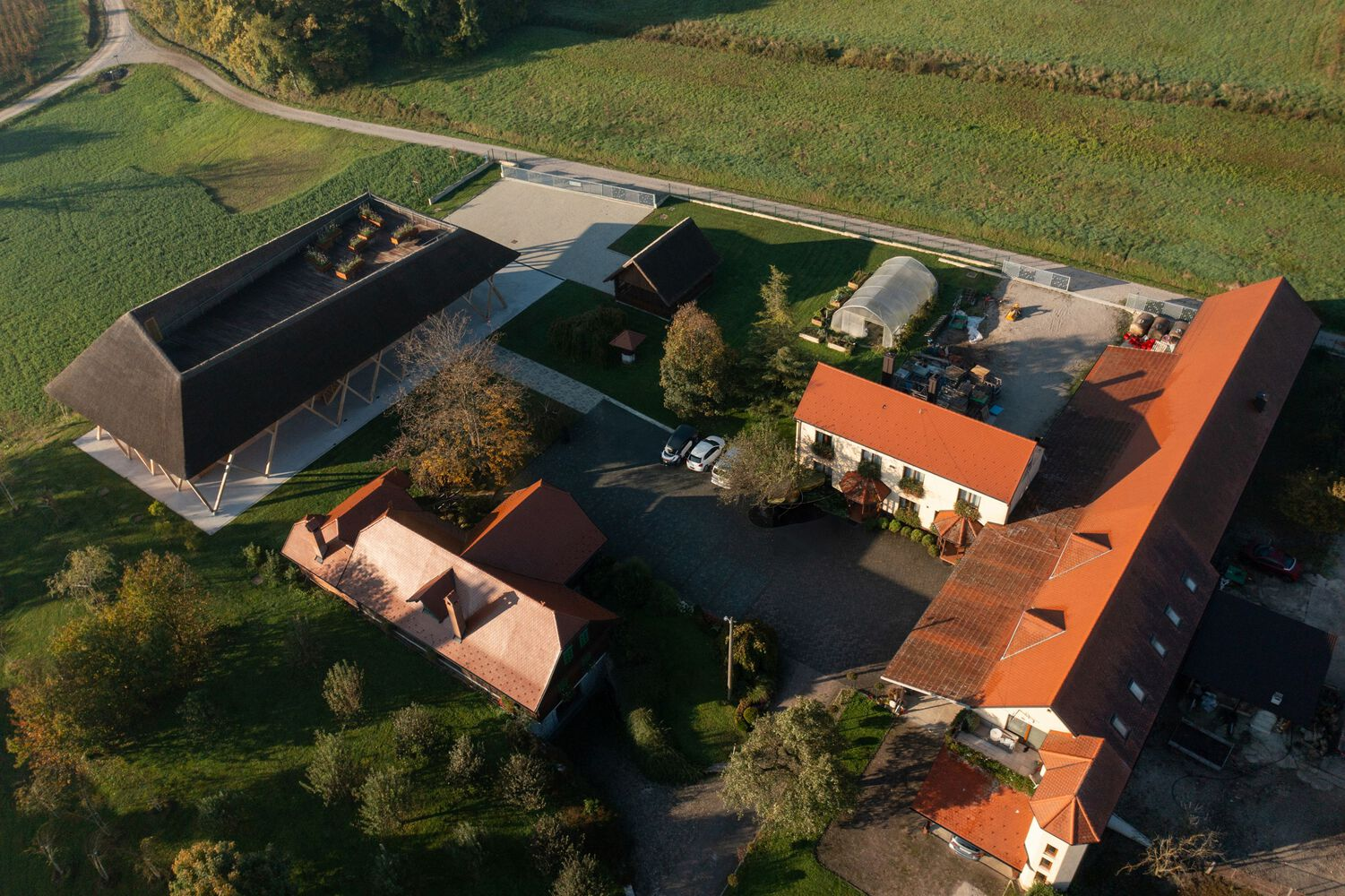 Drone view of the barn courtyard surrounded by existing farm buildings with terracotta roofs at sunset