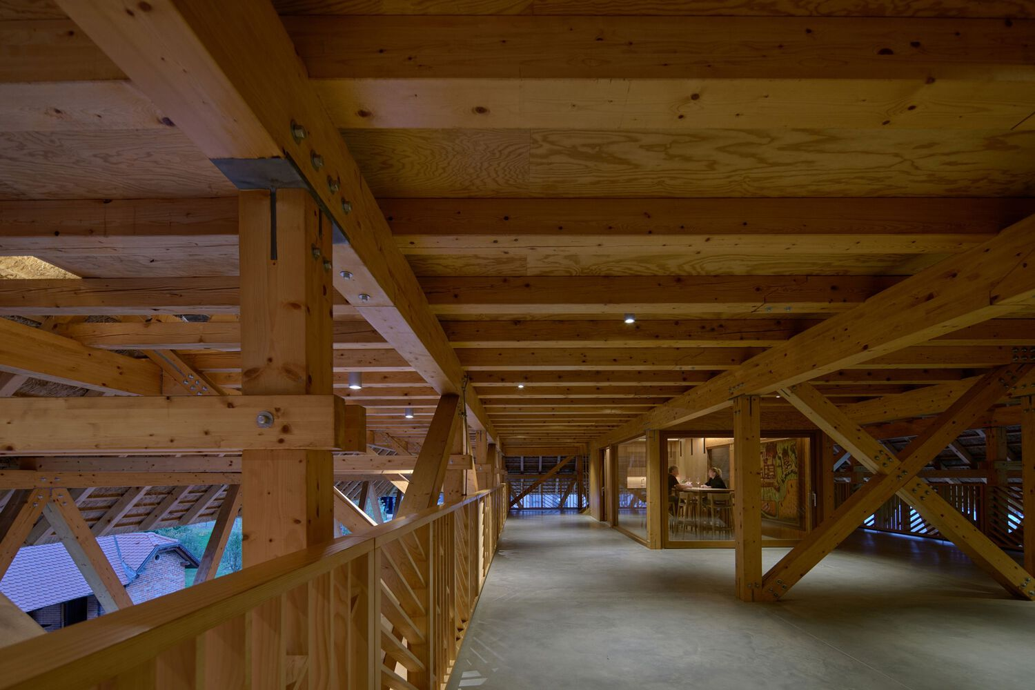 Interior corridor with exposed timber beams, joists, and cross-bracing under plywood ceiling panels