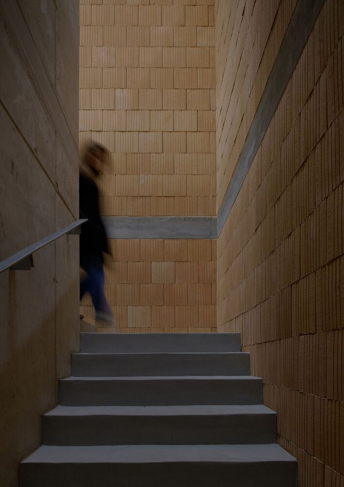 Concrete staircase ascending between textured brick walls with a figure in motion blur