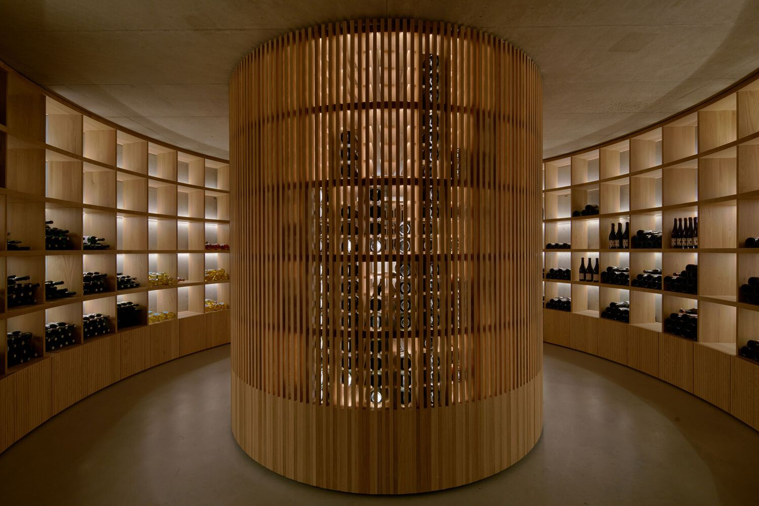 Cylindrical timber screen surrounding wine storage within a circular room with illuminated shelving