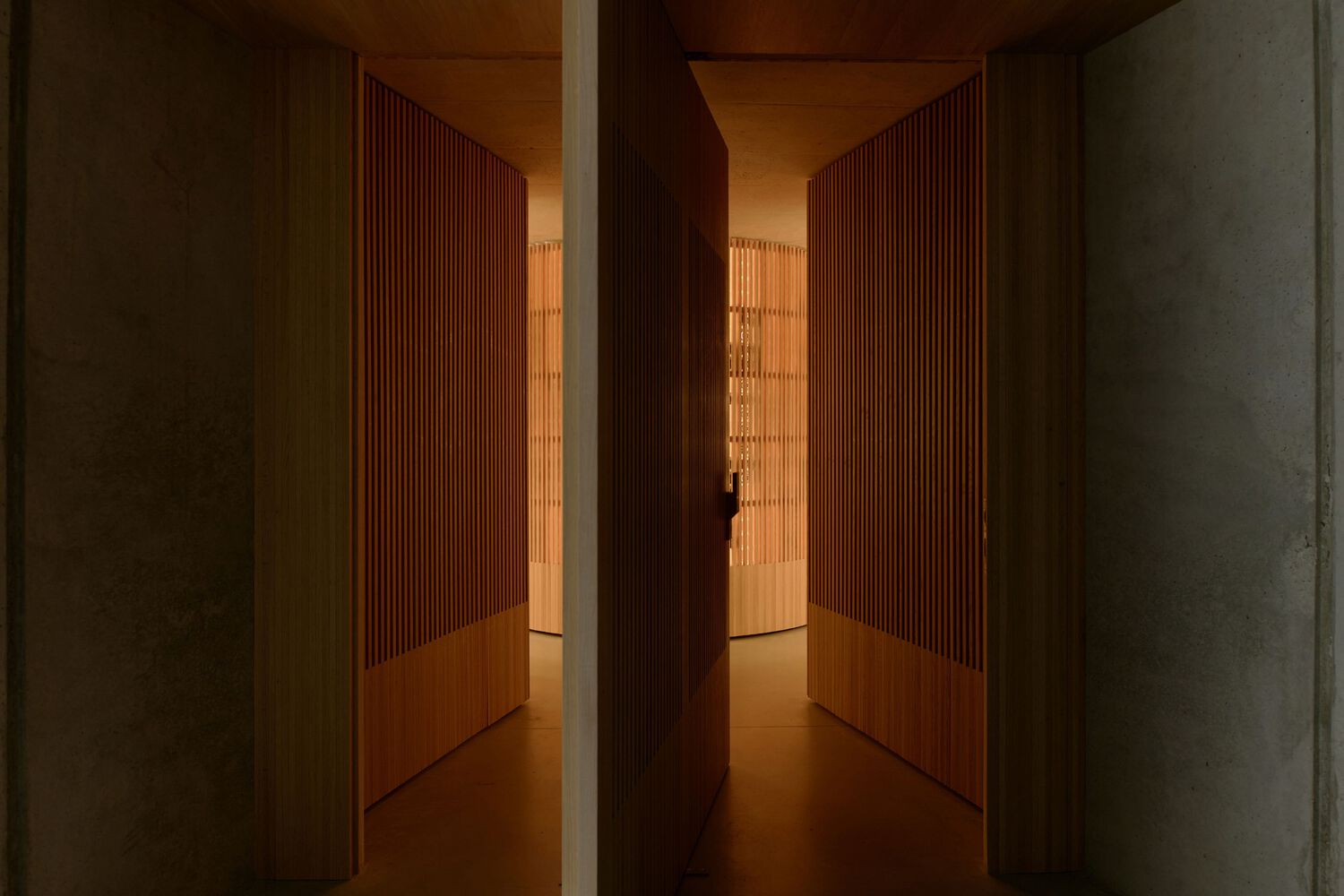 Narrow corridor with vertical timber slat walls and warm recessed lighting between concrete columns