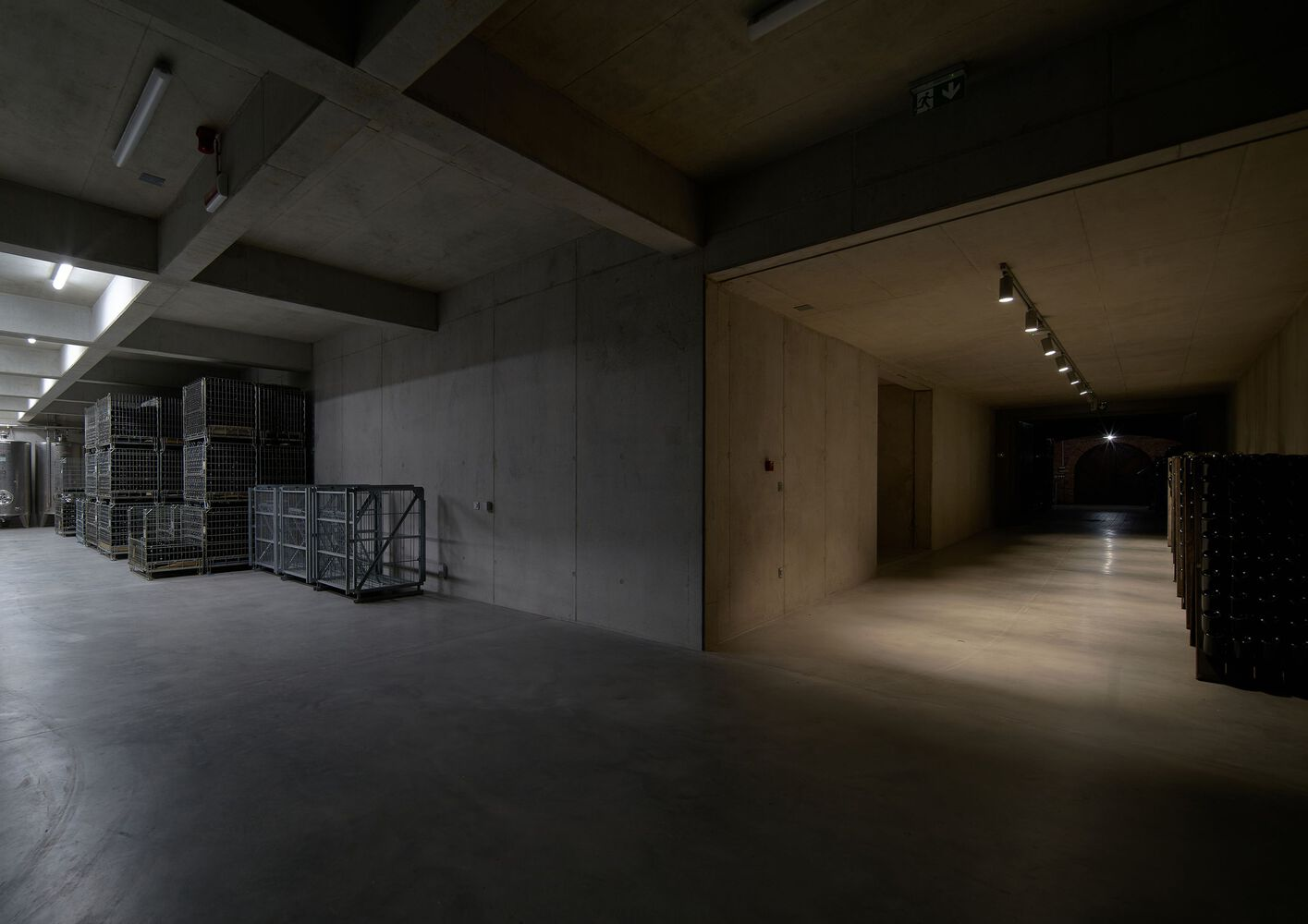 Basement corridor with exposed concrete columns and beams alongside metal storage cages and plywood-lined walls