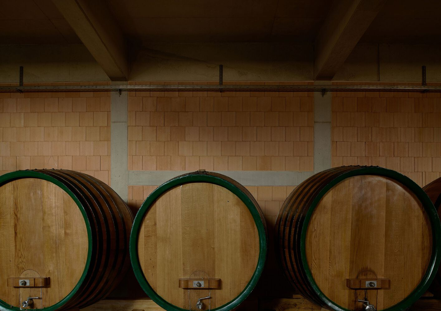 Row of large wine barrels against a ceramic tile wall with timber beams overhead