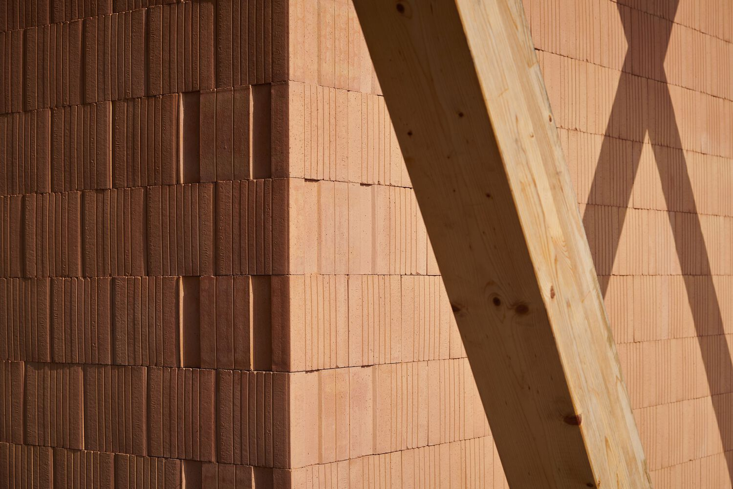 Terracotta tile wall with diagonal timber beam shadow cast across its textured surface