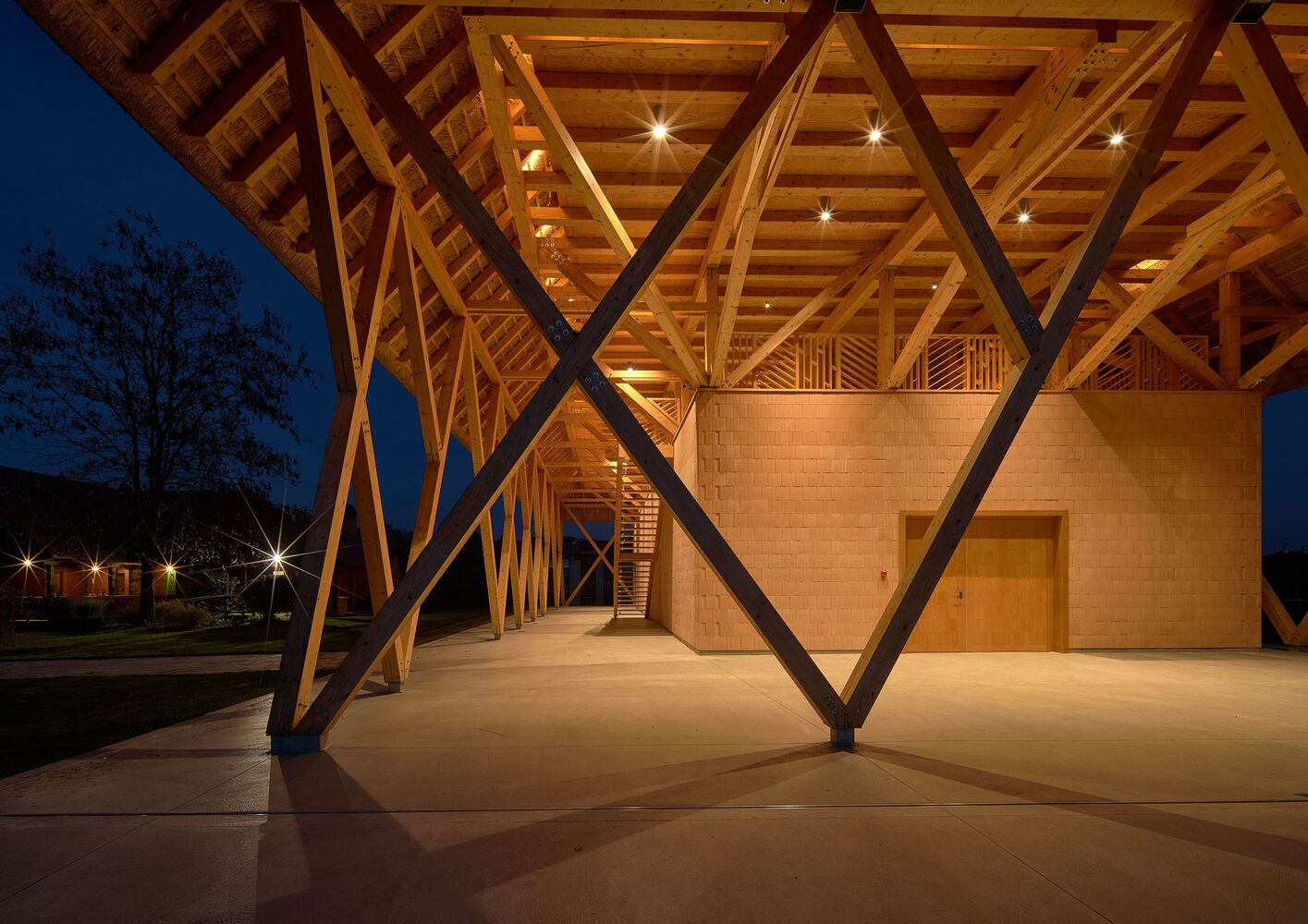 Covered entrance with exposed timber truss structure and steel diagonal bracing at dusk