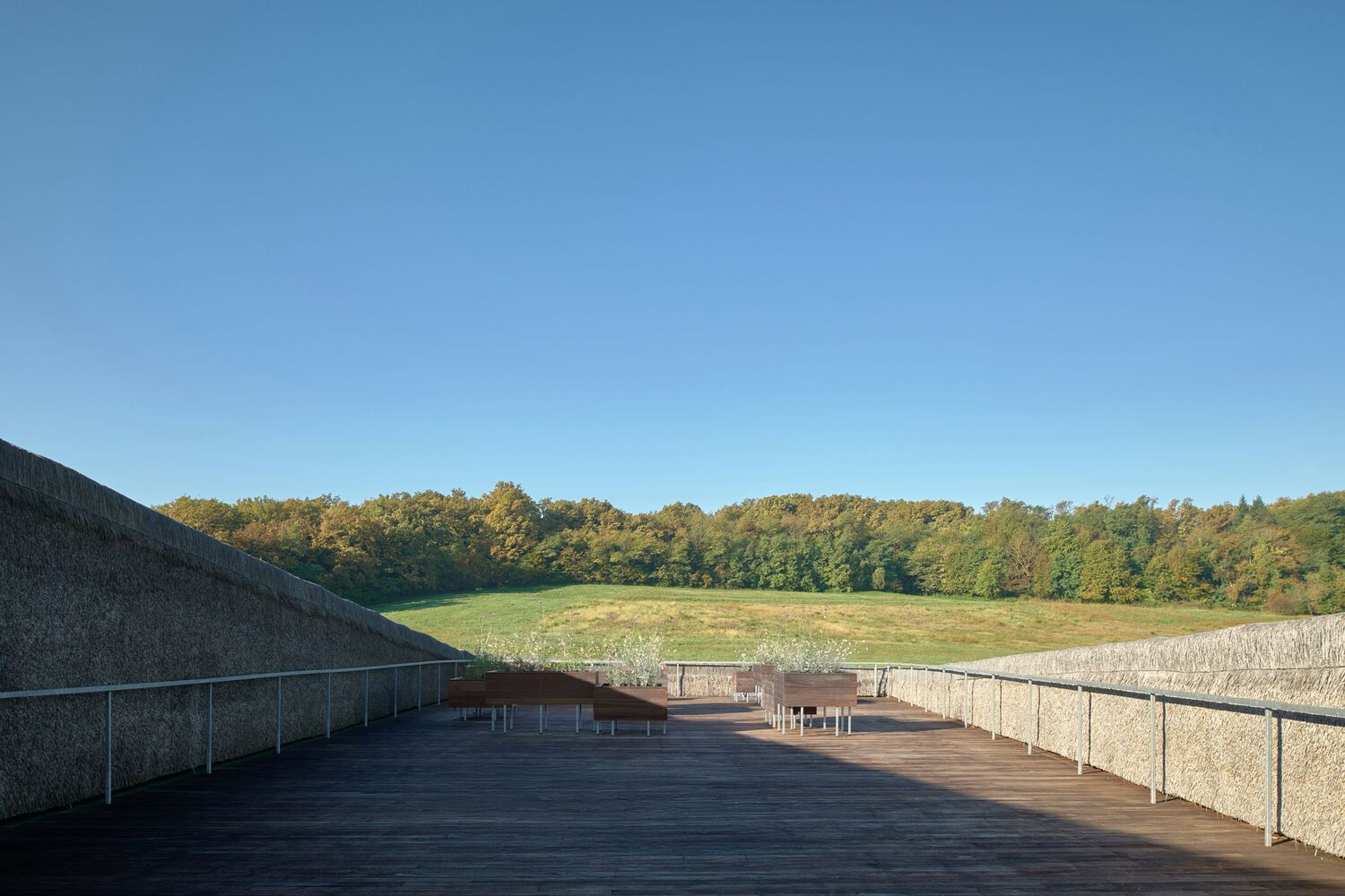 Rooftop terrace with dark decking and stone retaining walls overlooking a meadow and forest