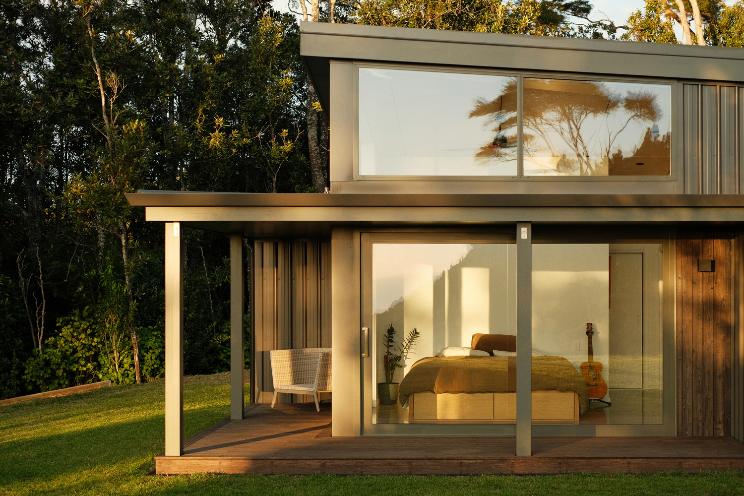 Two-storey bedroom wing with covered timber deck and full-height glazing at dusk