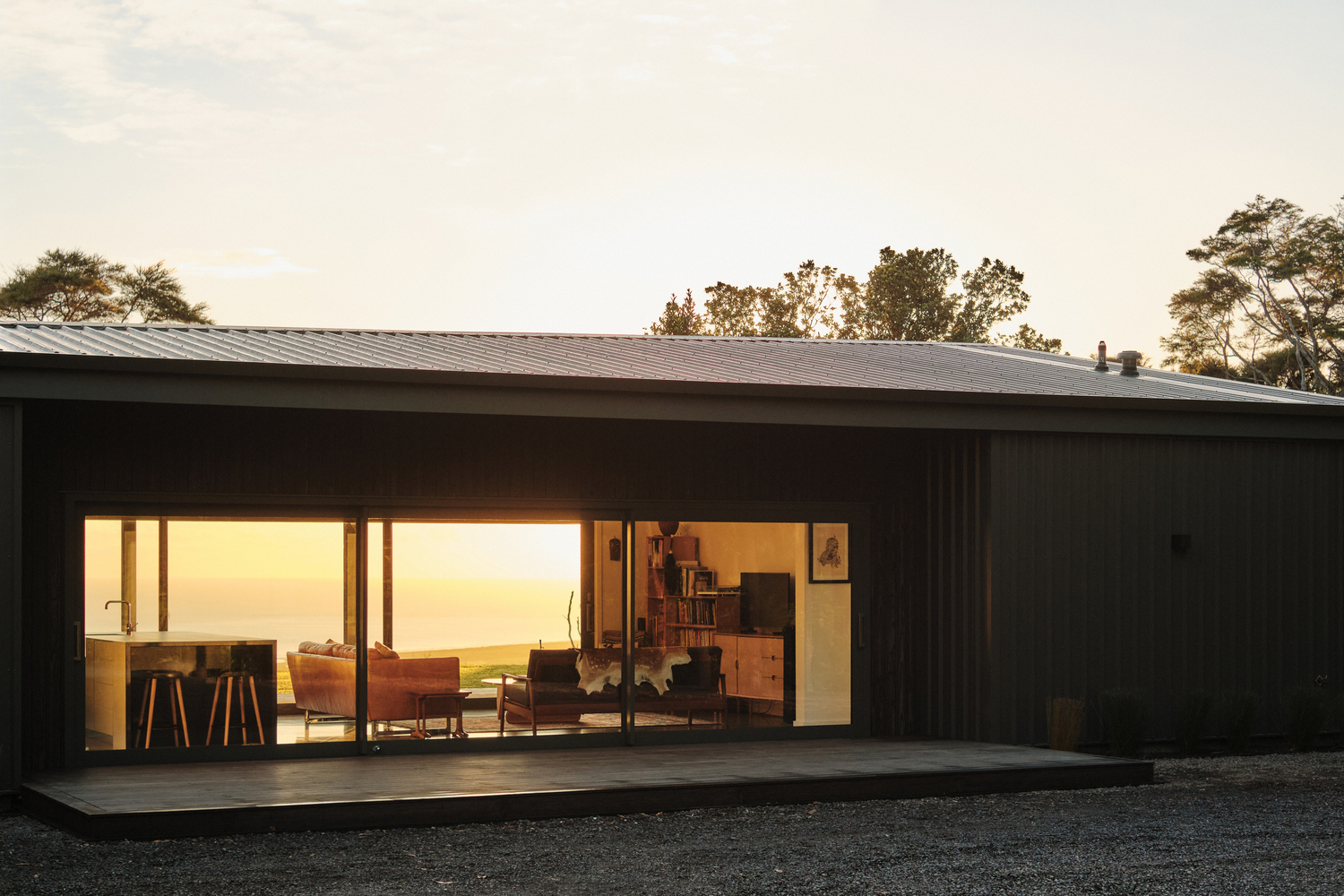 Living pavilion with black timber cladding and full-width glass opening at golden hour