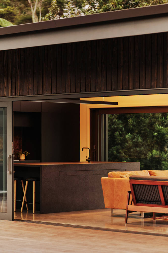 Covered timber deck with outdoor kitchen counter and dark vertical wood siding in afternoon light