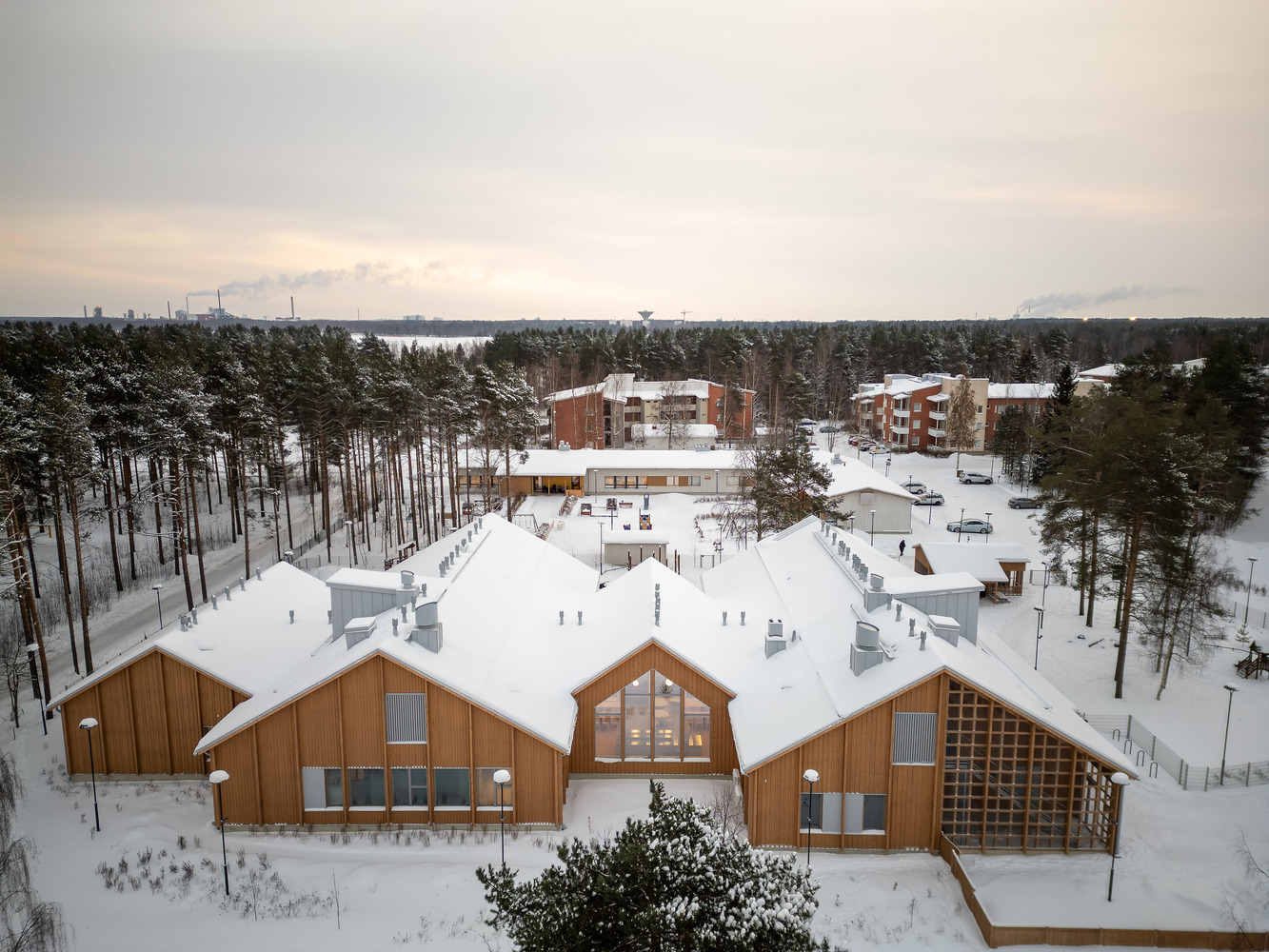 Aerial view of timber-clad gabled volumes with snow-covered roofs nestled among pine trees