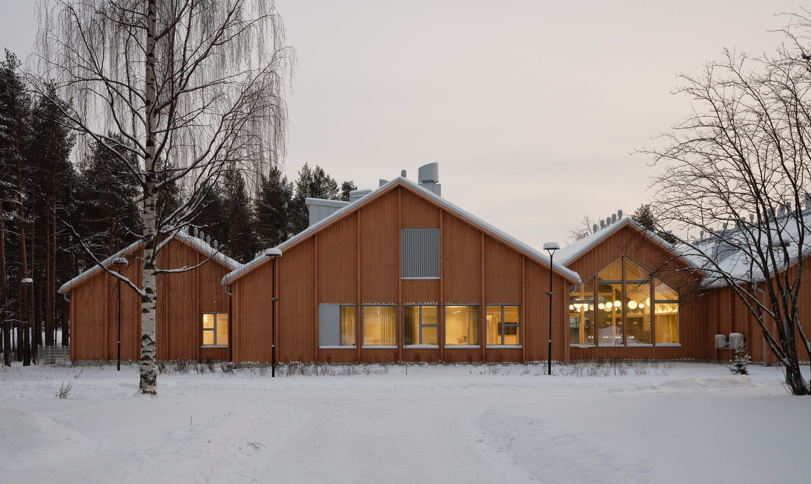 Courtyard facade with vertical timber cladding and warm interior lights glowing through glass at twilight